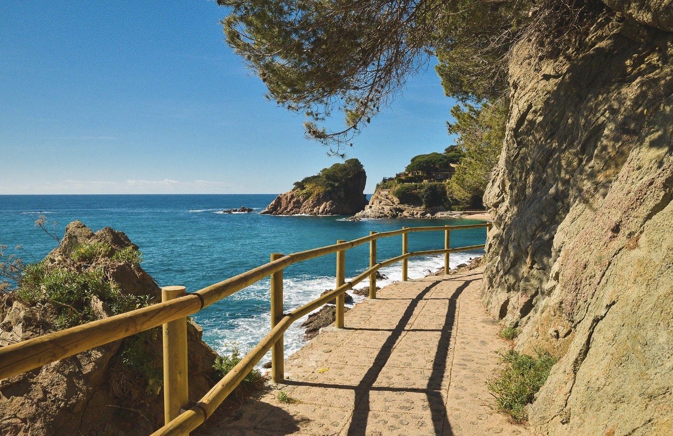 The paved Camí de Ronda coastal path winding above a turquoise bay on the Costa Brava